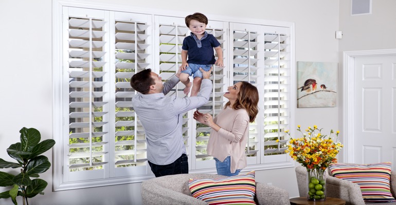 Parents Lifting Child In Front of Window Treatments